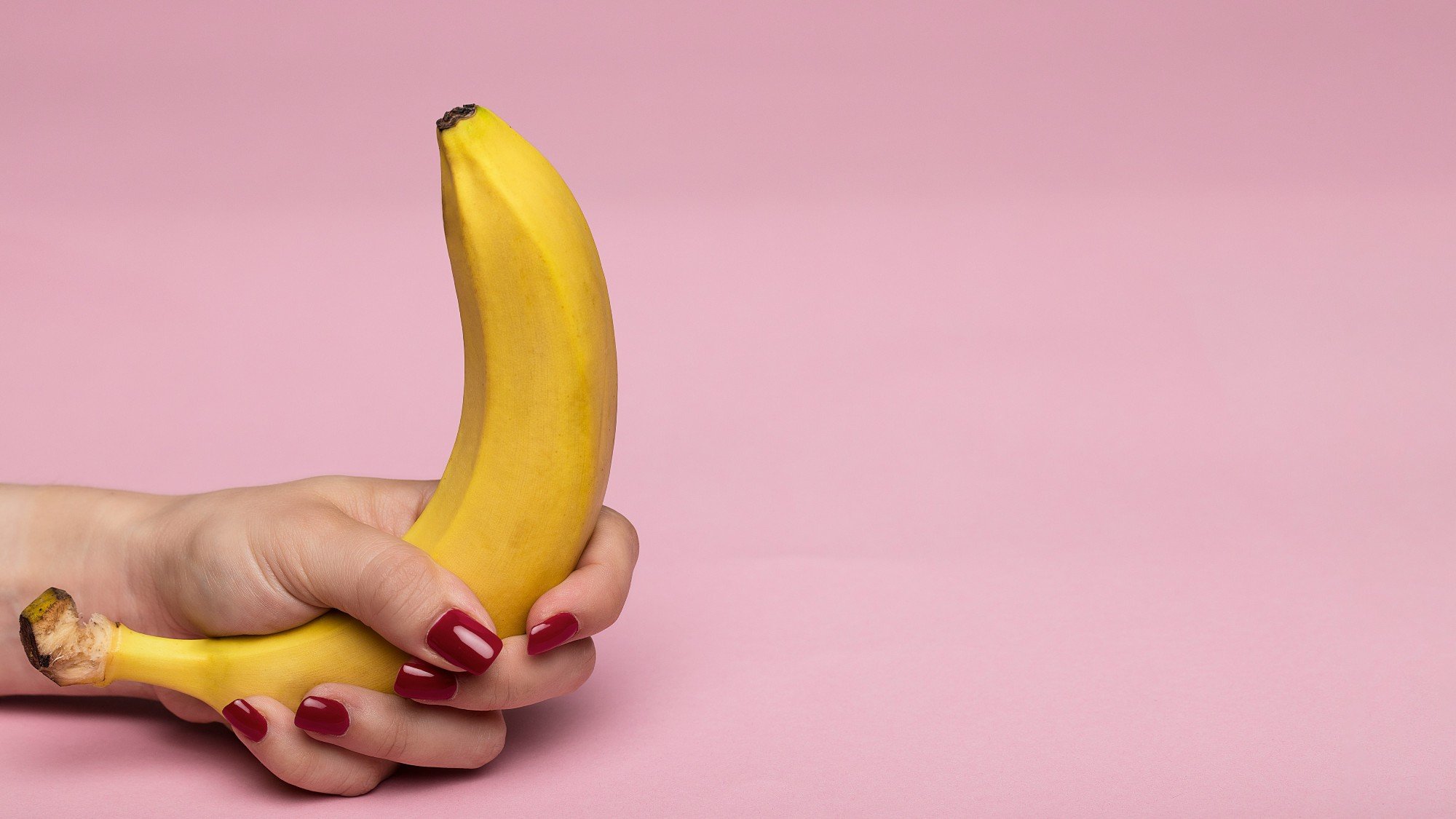 Symbolbild für Erektionsstörung: Eine Hand mit rot lackierten Fingernägeln hält eine Banane – metaphorische Darstellung im Kontext von Hezkue.