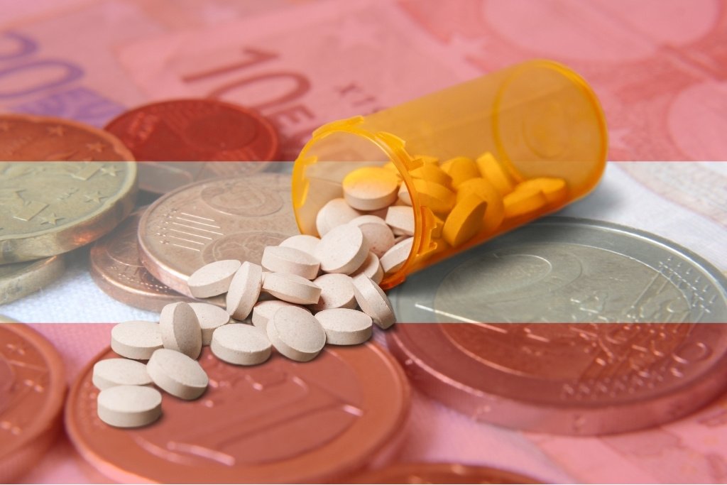 Euromünzen und Scheine mit einer transparent gehaltenen Österreich-Flagge im Vordergrund. Mittig ist ohne Transparenz eine ausgeschüttete Medikamentendose mit weißen Tabletten zu sehen.