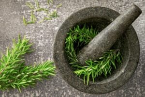 Obl Rosmarin Haarausfall bekämpfen kann, wird in diesem Artikel beantwortet. Frische Rosmarinzweige in einem dunklen Mörser, begleitet von einem Stößel. Die grünen Nadeln heben sich deutlich vom grauen Hintergrund und dem steinernen Mörser ab.