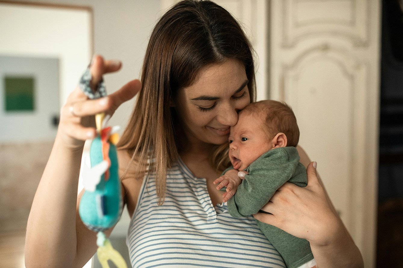 Haarausfall nach der Schwangerschaft: Junge Mutter hält ihr Neugeborenes sanft im Arm und schaut liebevoll auf es herab.