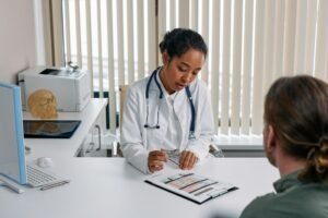 Eine Ärztin im Gespräch mit einem Patienten in mittlerem Alter. Es zeigt, dass das Ansprechen der Probleme der erste Schritt zu Hilfe bei Erektionsstörungen ist.