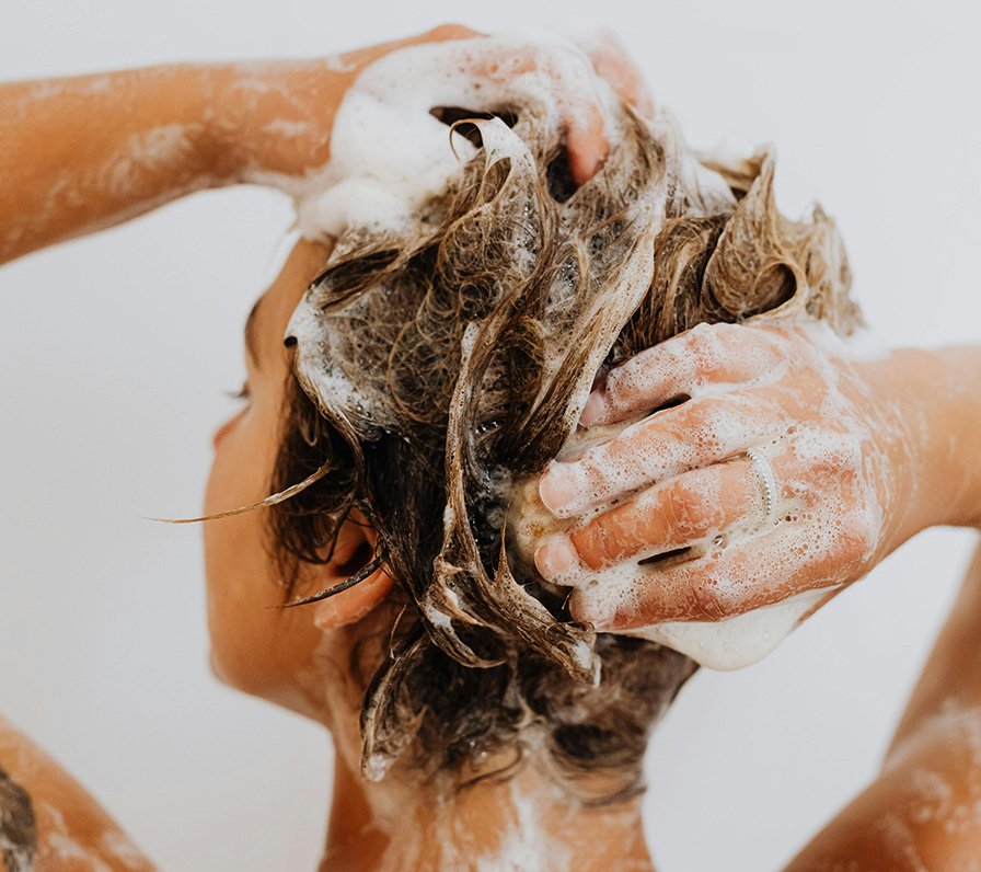 Person wäscht ihre Haare mit Shampoo, ein Konzeptbild für die Anwendung von Koffein gegen Haarausfall