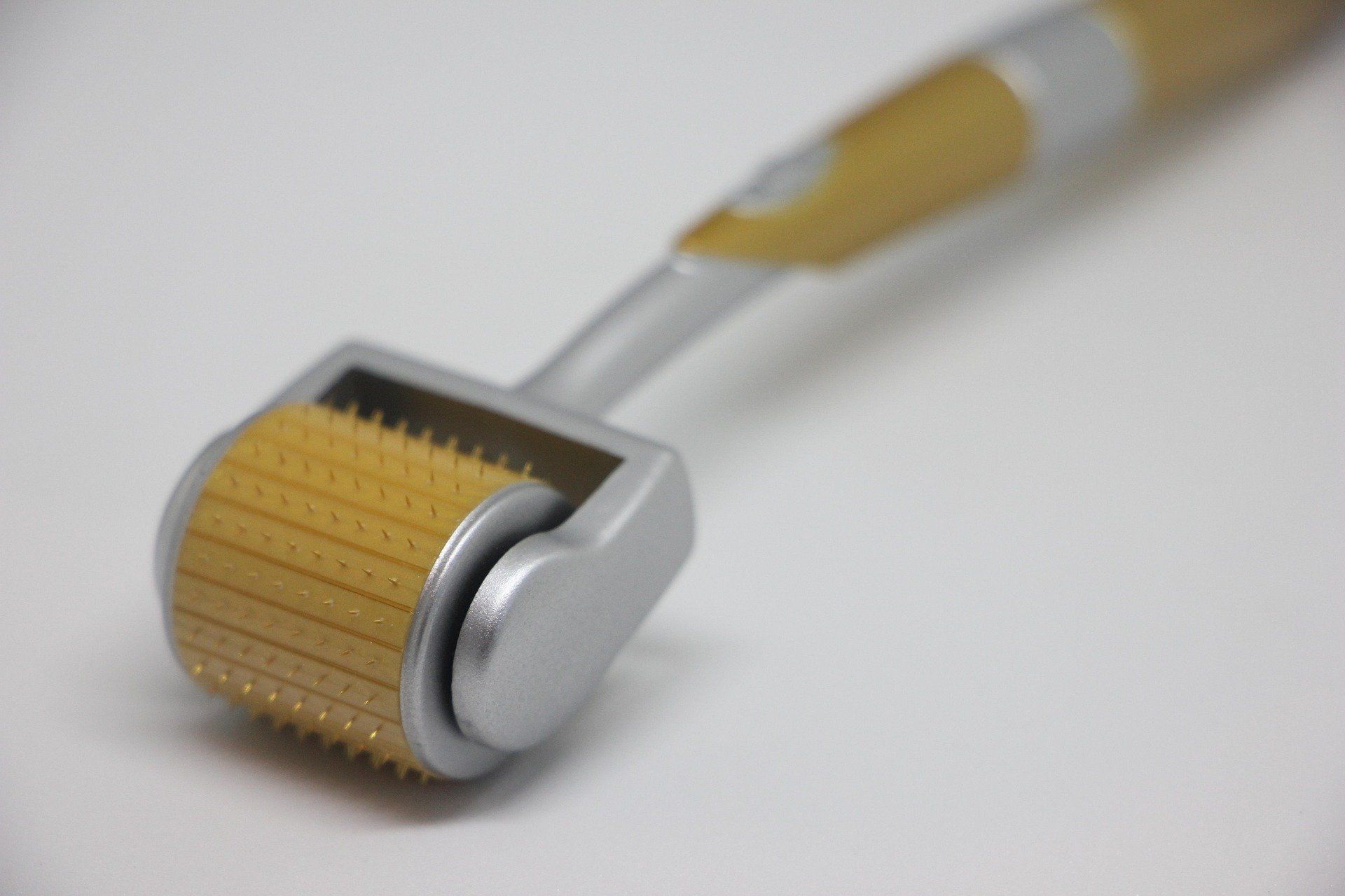 Ein gold-silberner Dermaroller mit feinen Nadeln, der für Microneedling-Behandlungen verwendet wird, liegt auf einer weißen Oberfläche