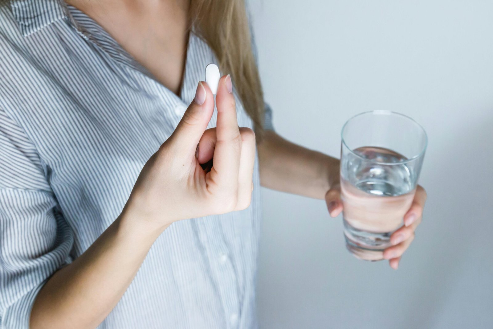 Eine Frau hält eine Tablette und ein Glas Wasser in den Händen. Es symbolisiert die Einnahme von Medikamenten in Off-label Nutzung, die zahlreiche zusätzliche Therapieoptionen ermöglicht.