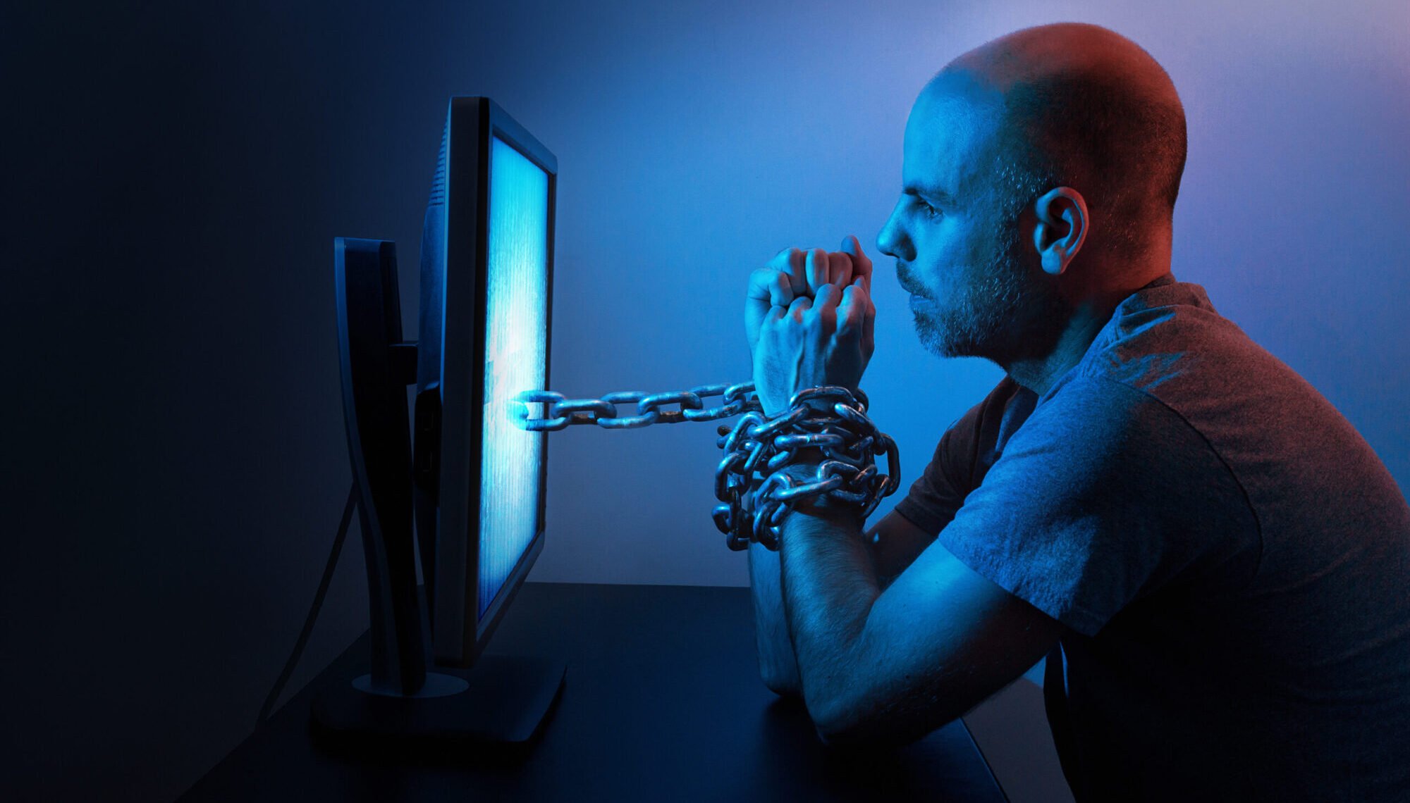 Ein Mann sitzt gefesselt vor einem Computerbildschirm, der seinen Pornokonsum symbolisiert. Die Ketten stehen für die Abhängigkeit und eine mögliche Erektionsstörung durch Pornos.